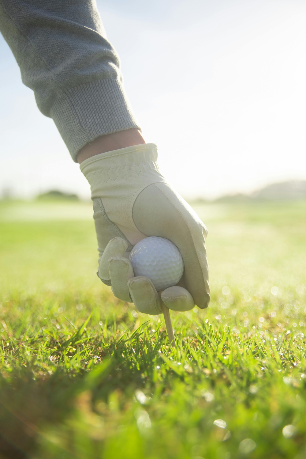 Imagen de pelota de golf sobre el tee con la mano de un golfista